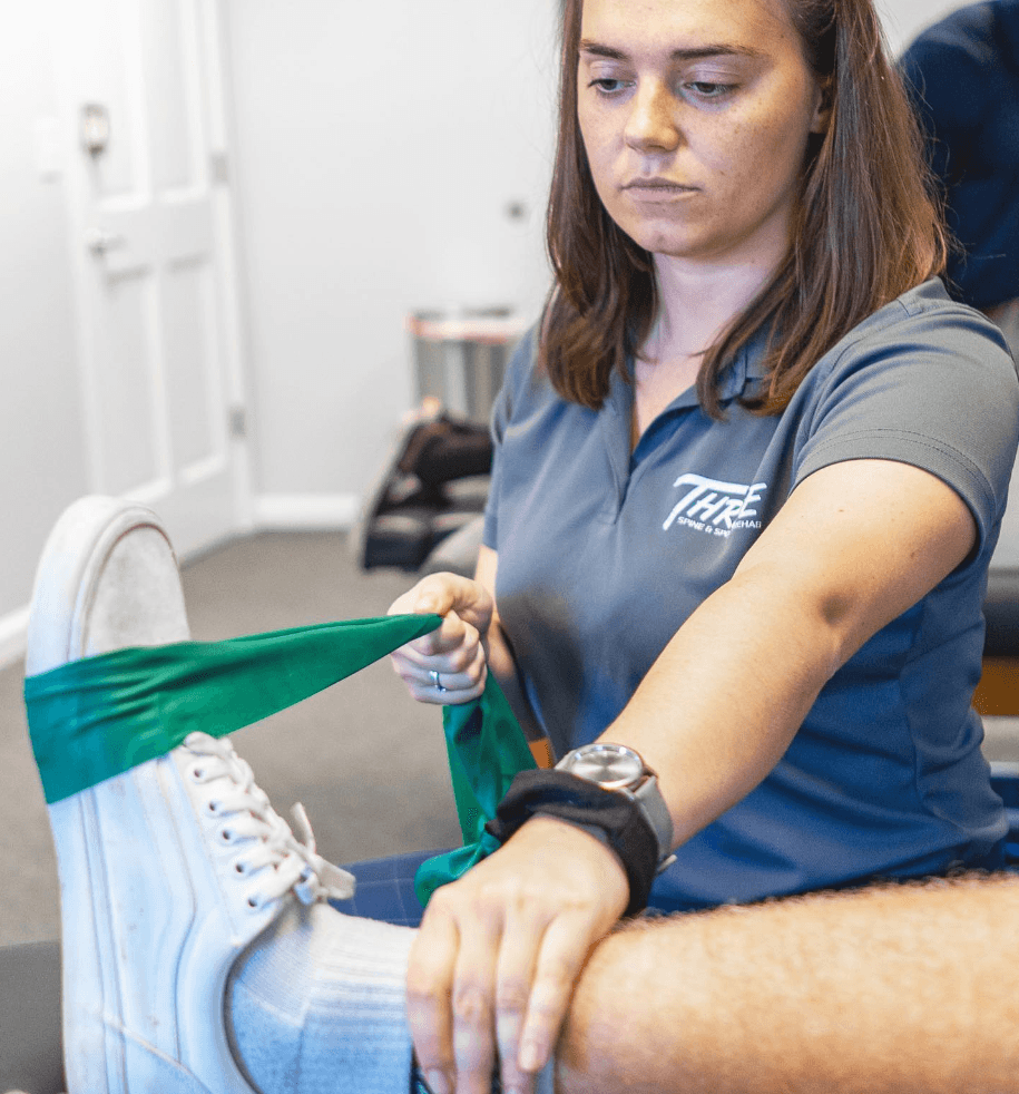 Male therapist in a black Thrive polo guiding a patient’s bent knee through a controlled stretch.