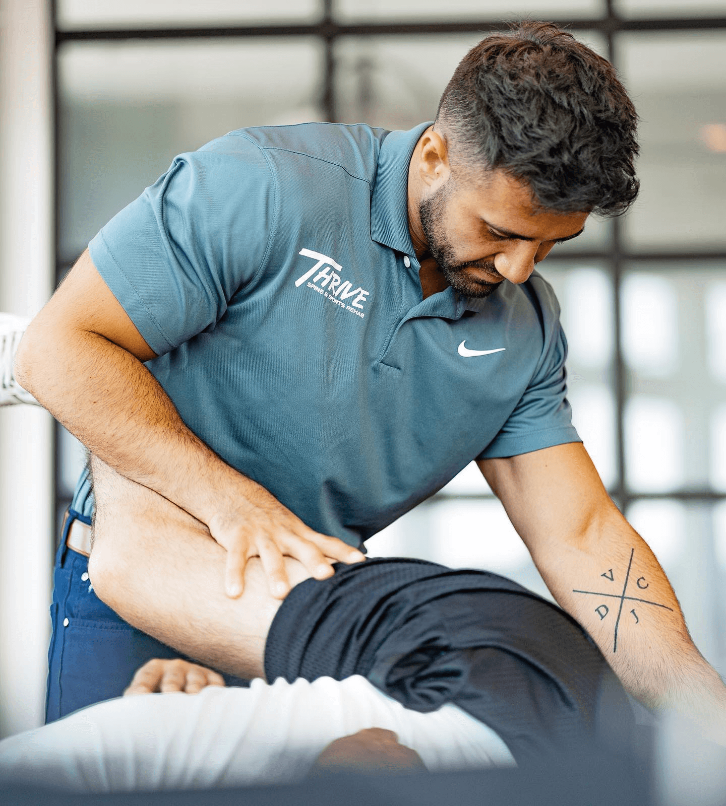 Chiropractor in a Thrive polo treating the hip and lower back of a patient lying face down